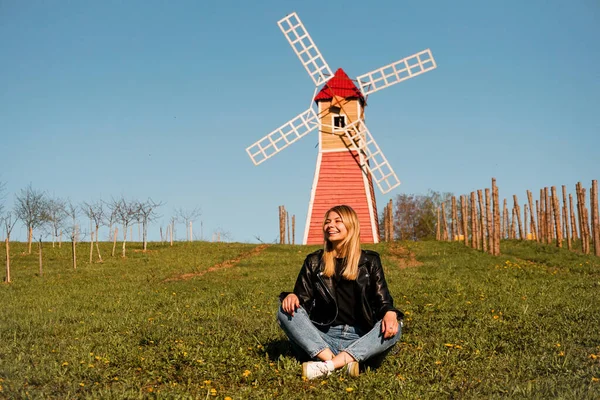 Belle jeune femme assise sur l'herbe sur le fond du moulin — Photo