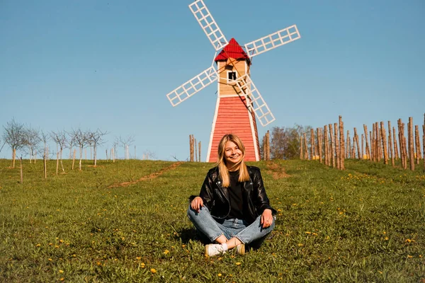 Belle jeune femme assise sur l'herbe sur le fond du moulin — Photo