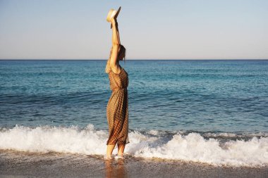 Kahverengi elbiseli ve hasır şapkalı bir kadın. Kumsalda tatil.