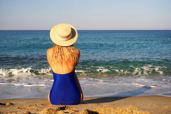 Молодая женщина загорает на тропическом пляже. Женщина в синем купальнике и шляпе — стоковое фото