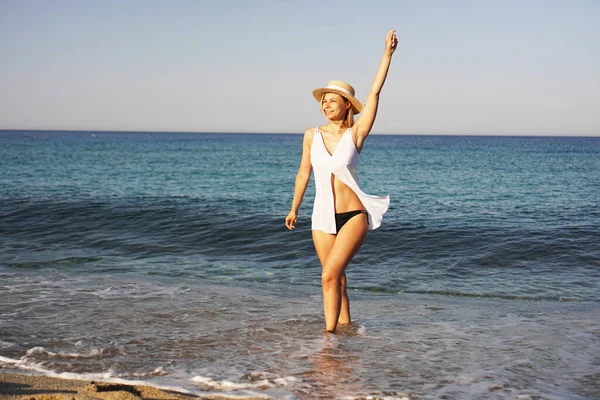 Flickan går på stranden. Vacker blond kvinna i vit blus och halmhatt — Stockfoto