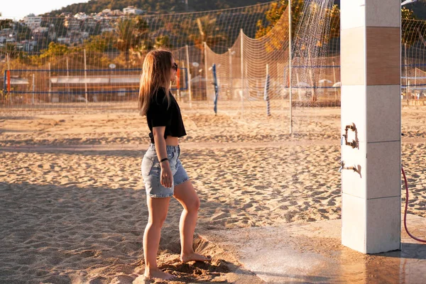 Девушка в шортах и черная футболка на пляже возле душа. — стоковое фото