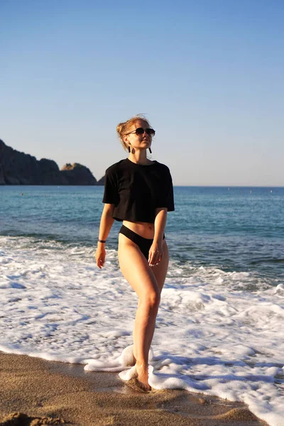 Νεαρή γυναίκα με μαύρο μπλουζάκι και εσώρουχα στην παραλία. — Φωτογραφία Αρχείου
