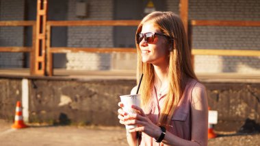 Dışarıda elinde bir bardak limonata olan genç bir kadın. Güneşli bir gün ve şehir yemekhanesi