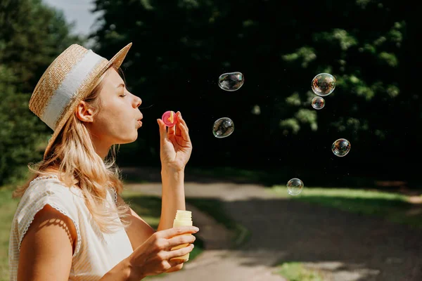 Leuke blonde vrouw die zeepbellen blaast. Mooi groen park op achtergrond — Stockfoto