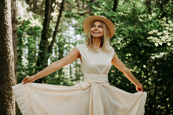 Mujer joven con sombrero de paja sosteniendo el dobladillo de su vestido blanco — Foto de Stock