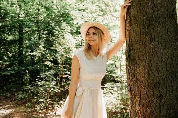 一位戴着草帽，穿着时髦衣服的漂亮姑娘站在一棵树旁的公园里 — 图库照片