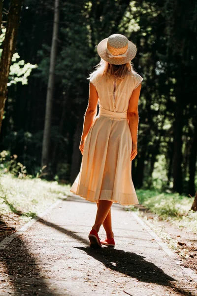 Uma jovem mulher em um vestido branco e um chapéu de palha caminha pela floresta — Fotografia de Stock