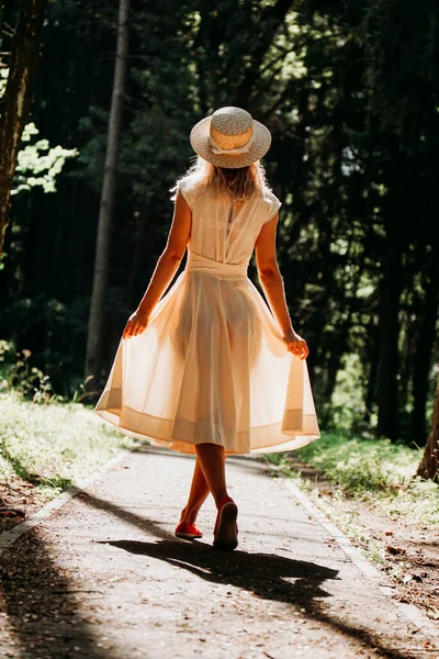 Mladá žena v bílých šatech a slamáku kráčí lesem — Stock fotografie