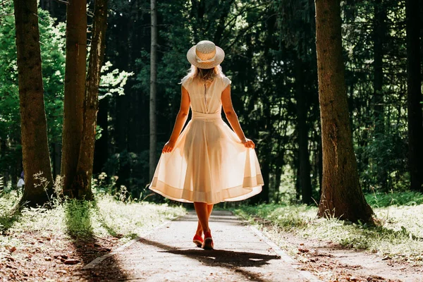 Una giovane donna vestita di bianco e un cappello di paglia cammina nel bosco — Foto Stock