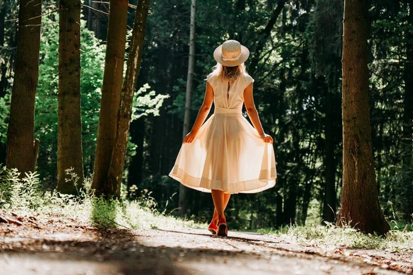 Eine junge Frau in weißem Kleid und Strohhut geht durch den Wald — Stockfoto