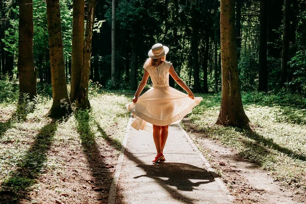 Uma jovem mulher em um vestido branco e um chapéu de palha caminha pela floresta — Fotografia de Stock