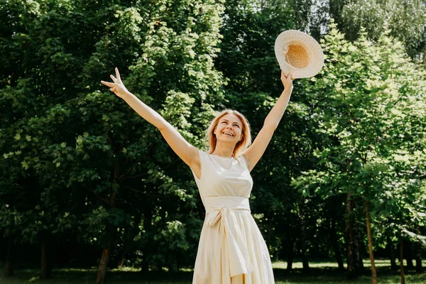 Bella giovane donna con cappello di paglia e vestito bianco in un parco verde — Foto Stock