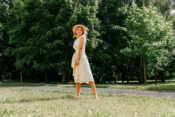 Schöne junge Frau mit Strohhut und weißem Kleid in einem grünen Park — Stockfoto