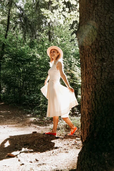 Дівчина в білій сукні і капелюсі проходить через літній парк або ліс — стокове фото