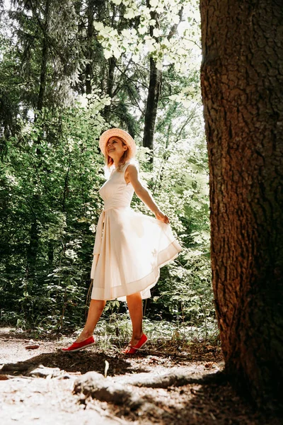 Una ragazza in abito bianco e cappello cammina attraverso un parco estivo o una foresta — Foto Stock