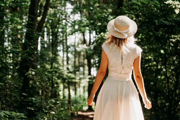 Bella giovane donna con cappello di paglia e vestito bianco in un parco verde — Foto Stock