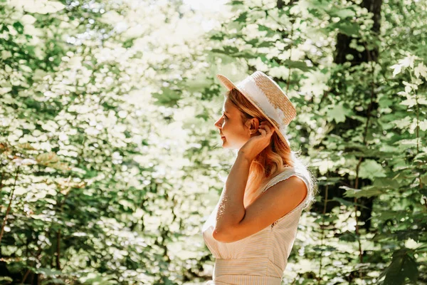 美丽的年轻女子戴着草帽，穿着白色衣服，站在绿地里 — 图库照片