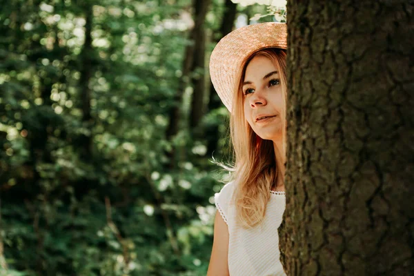 Porträt eines jungen Mädchens im Wald. Sie lugt hinter einem Baumstamm hervor — Stockfoto