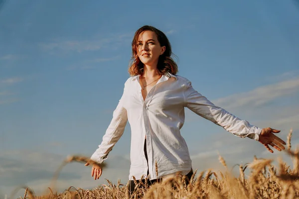 Buğday tarlasında beyaz gömlekli mutlu bir genç kadın. Güneşli bir gün. — Stok fotoğraf