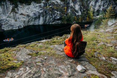 Girl tourist looks at mountain lake in Marble Canyon. Autumn in Karelia, Russia clipart