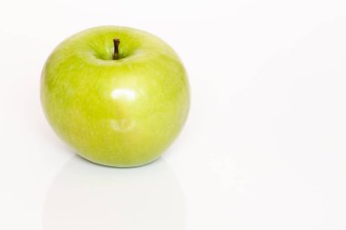 Yeşil bir elma, olgun ve sulu, beyaz bir masada.