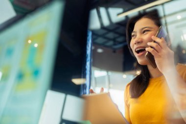 Yaratıcı ajans Asyalı kadın günlük kıyafet sohbeti. Akıllı telefon serbest bilgisayar ile birlikte çalışma alanındaki ofis alanında çalışıyor. Ofis geçmişi bulanık.