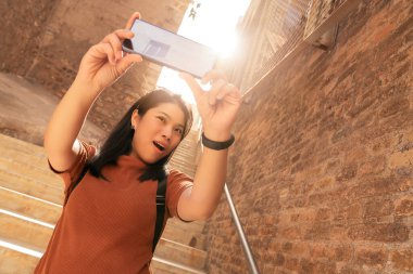 Çekici Asyalı kadın gezgin turist el akıllı telefon kullanır. Video çeker. Cartagena İspanya 'daki eski taş merdiven koridorunu gezer.