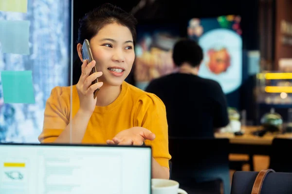 creative agency asian female casual cloth conversation with smartphone freelance working wuth laptop at coworking area office space with freshness with blur office background