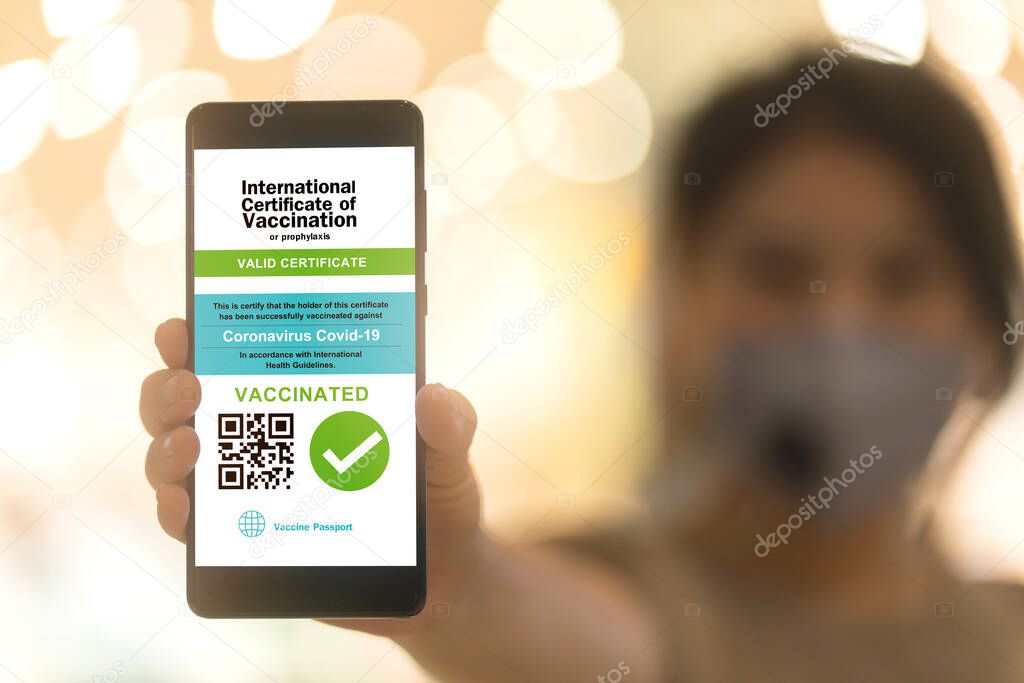 Smartphone displaying a valid digital vaccination certificate passport for COVID-19 in female's hand, public area background. Vaccination, disease immunity passport, health and safty travel concepts