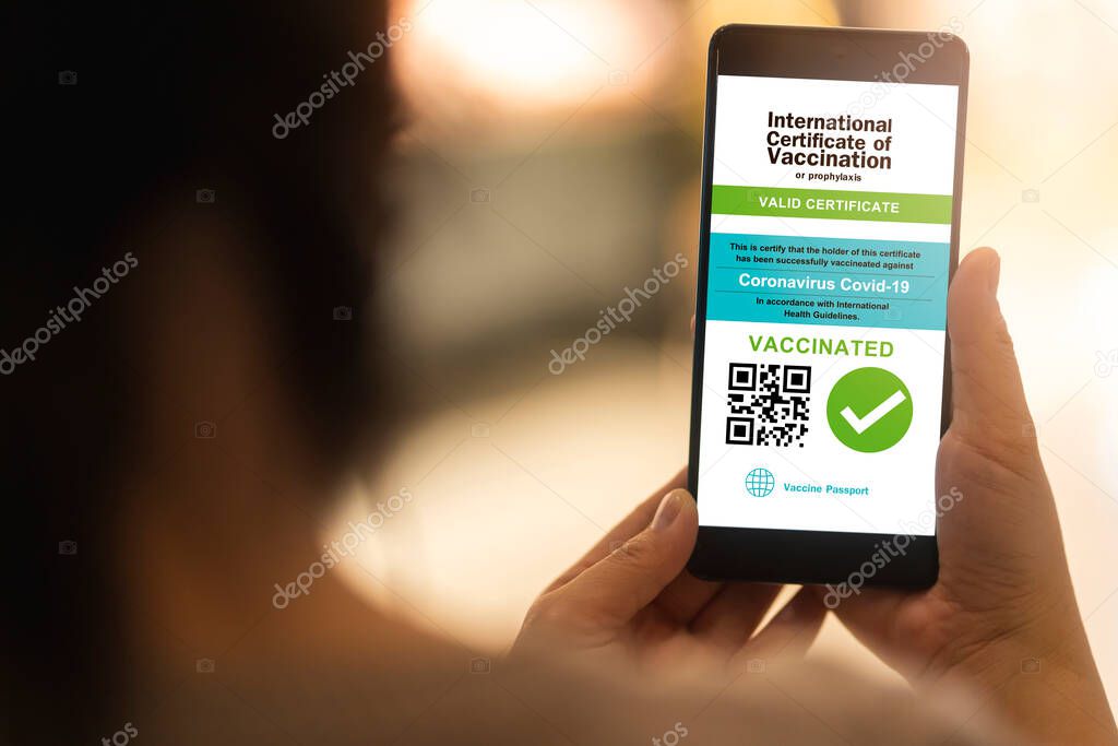 Smartphone displaying a valid digital vaccination certificate passport for COVID-19 in female's hand, public area background. Vaccination, disease immunity passport, health and safty travel concepts