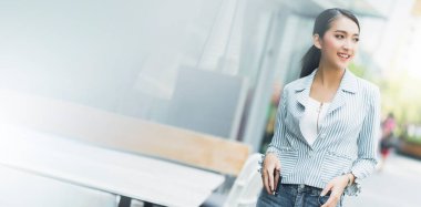 Zeki, zarif Asyalı kadın, kendine güvenen, şehir bahçesi afişlerinin arka planında yürüyen, iş insanlarının fikirlerine orantılı bir şekilde gülümsüyor.