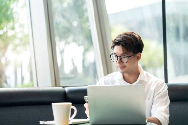 Zeki, çekici, pozitif Asyalı iş adamı gözlüklü, uzaktan kumandalı, yeni normal yaşam tarzı el bilgisayarı kullanan uzaktan kumandalı televizyon konferansında uzaktan kumandalı iş fikirleriyle buluşuyor.