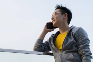 Çekici, zeki Asyalı, serbest giyinen, rahat giyinen, akıllı telefon iletişimiyle güler yüzlü, kendinden emin, teknoloji fikirleri üreten erkek.