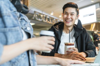 Mutlu Asyalı çift, internetten internette sörf yaparken maskesini çıkarıyor. Restoranda dokunmatik ekran bilgisayarına bakan genç bir adam ve kadın birlikte gülüyorlar.