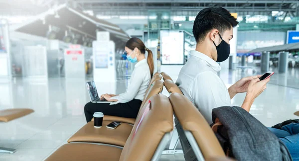 Social distancing, businessman wearing face mask sit working with laptop keeping distance away from each other to avoid covid19 infection during pandemic. Empty chair seat red cross shows new normal