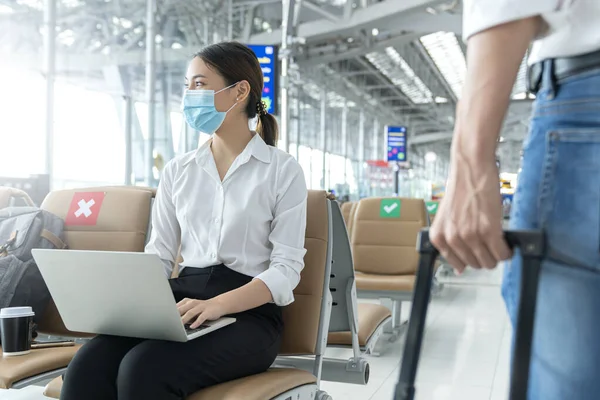 Social distancing, businesswoman wearing face mask sit working with laptop keeping distance away from each other to avoid covid19 infection during pandemic. Empty chair seat red cross shows new normal