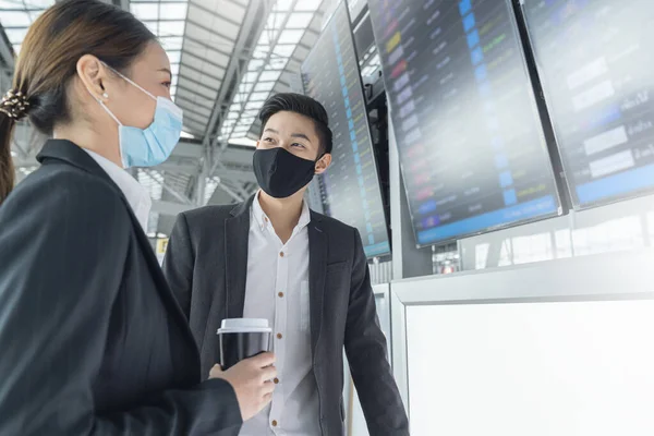 国際空港ターミナルで顔マスク保護を持つ2人のアジア人ビジネスマンとビジネスマンボードビジネスコンセプトに近い会話 — ストック写真