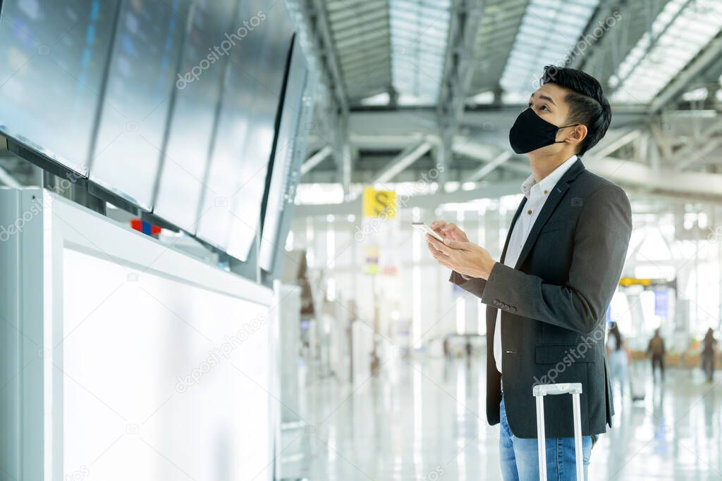 asian business people wear mask face protection business travel checking map and flight schedule at information boarding screen in terminal airport