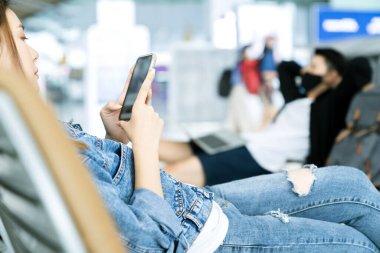 Güvenli seyahat için Asyalı çift koruyucu yüz maskesi takıyor bekle sosyal mesafeli yeni bir ahlak anlayışı ile rahatla ve havaalanından ayrılma terminalinde programlama için akıllı telefon ve laptop kullan