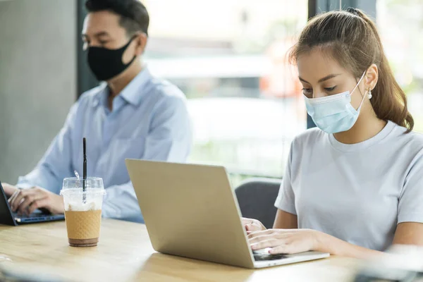 new normal lifestyle concept business people wearing mask sit with social distancing working in public area or co working space with laptop and smartphone