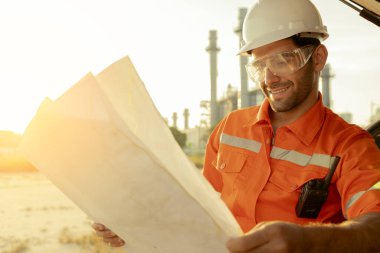 Beyaz tenli mühendis, endüstriyel işçiler güvenli üniformalar giyip telsiz ve dizüstü bilgisayarla elektrik santrali geçmişi olan bir arabada inceleme yapıyorlar.