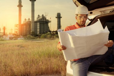 Beyaz tenli mühendis, endüstriyel işçiler güvenli üniformalar giyip telsiz ve dizüstü bilgisayarla elektrik santrali geçmişi olan bir arabada inceleme yapıyorlar.