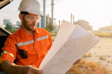 Beyaz tenli mühendis, endüstriyel işçiler güvenli üniformalar giyip telsiz ve dizüstü bilgisayarla elektrik santrali geçmişi olan bir arabada inceleme yapıyorlar.