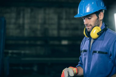 Kafkasyalı mühendis güvenli mavi kask takıyor ve fabrika atölyesinin arka planında üniforma giyiyor.