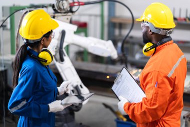 Mühendis erkek ve kadın teknisyen bakım kontrolü robot kol sistemini tablet dizüstü bilgisayarla kaynak yaparak işletim sürecinin kalitesini kontrol altına alıyor ağır endüstri 4.0 üretim fabrikası