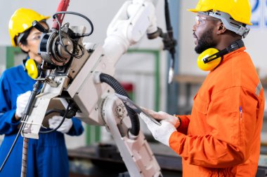 Mühendis erkek ve kadın teknisyen bakım kontrolü robot kol sistemini tablet dizüstü bilgisayarla kaynak yaparak işletim sürecinin kalitesini kontrol altına alıyor ağır endüstri 4.0 üretim fabrikası