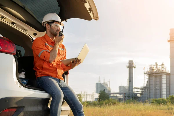 Beyaz tenli mühendis, endüstriyel işçiler güvenli üniformalar giyip telsiz ve dizüstü bilgisayarla elektrik santrali geçmişi olan bir arabada inceleme yapıyorlar.