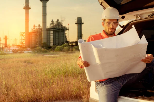 Beyaz tenli mühendis, endüstriyel işçiler güvenli üniformalar giyip telsiz ve dizüstü bilgisayarla elektrik santrali geçmişi olan bir arabada inceleme yapıyorlar.