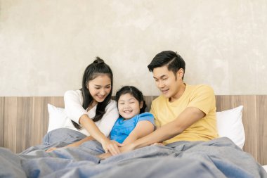 Genç Asyalı mutlu aile babası anne ve küçük kızı yatakta birlikte eğleniyorlar, birlikte eğleniyorlar aile içi ilişki anı konsepti.